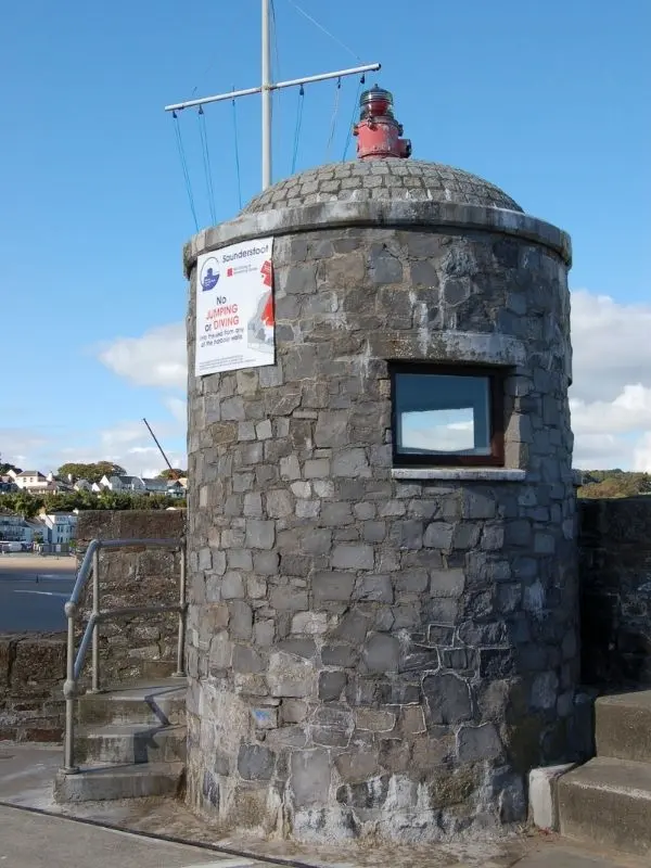 Saundersfoot Lighthouse close view with signs and blue sky in the background.